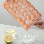 Pink silicone ice cube tray with round compartments, held by hands on a light gray background.